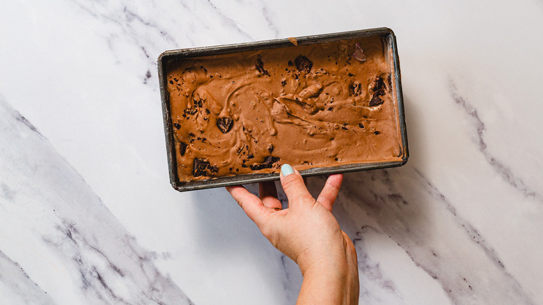 Hand holding frozen chocolate ice cream in container