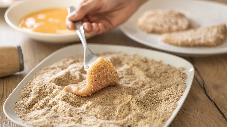 Person coating chicken cutlet in seasoned bread crumbs on a plate