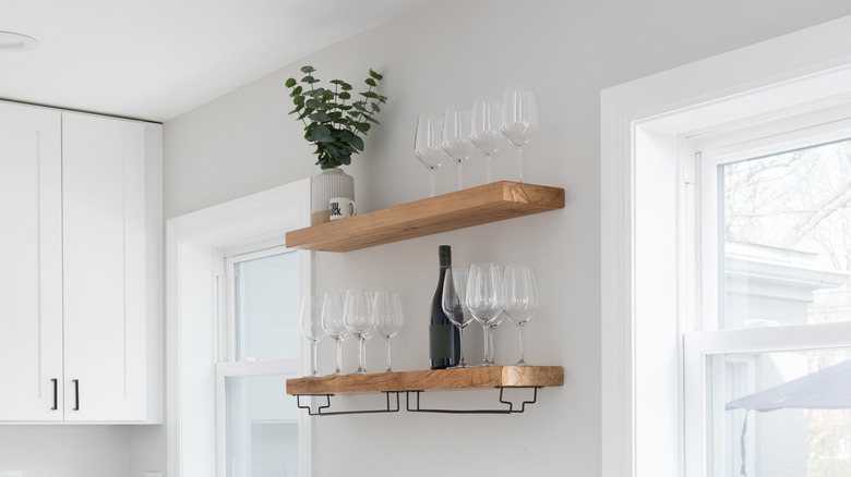 Wooden floating shelves holding wine glasses in the kitchen