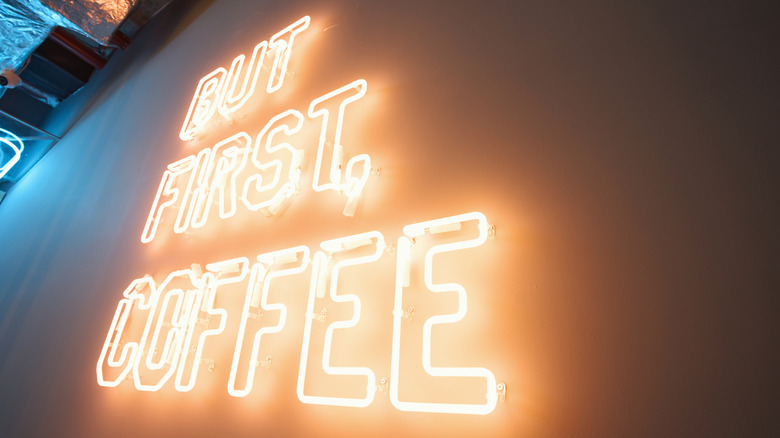 A white neon sign reading "But First, Coffee"