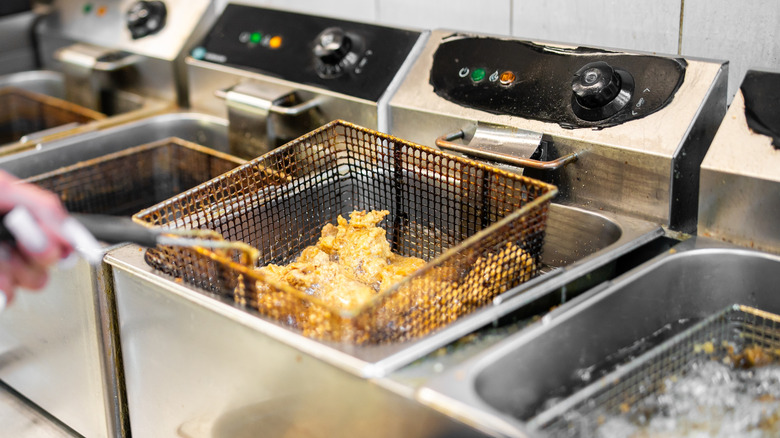 A basket of fried food is lifted out of a deep fryer