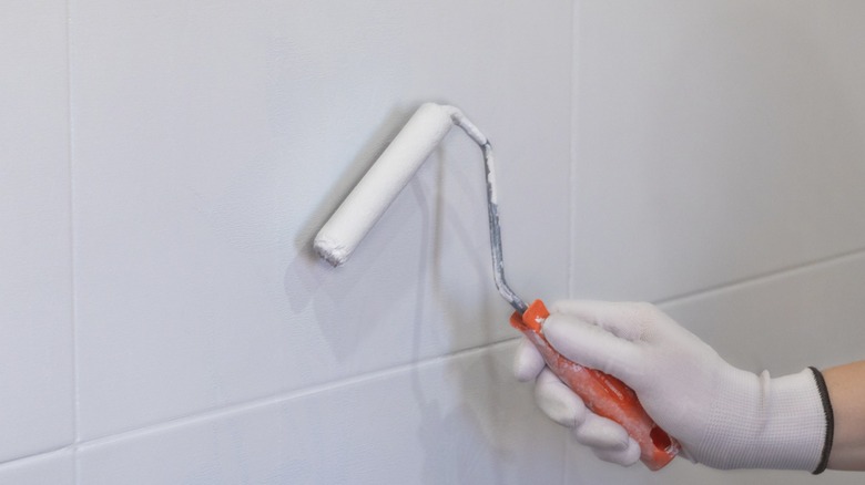 a gloved hand using a paint roller to paint tile white