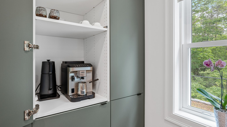 A coffee pot and espresso maker stored in a custom kitchen cabinet
