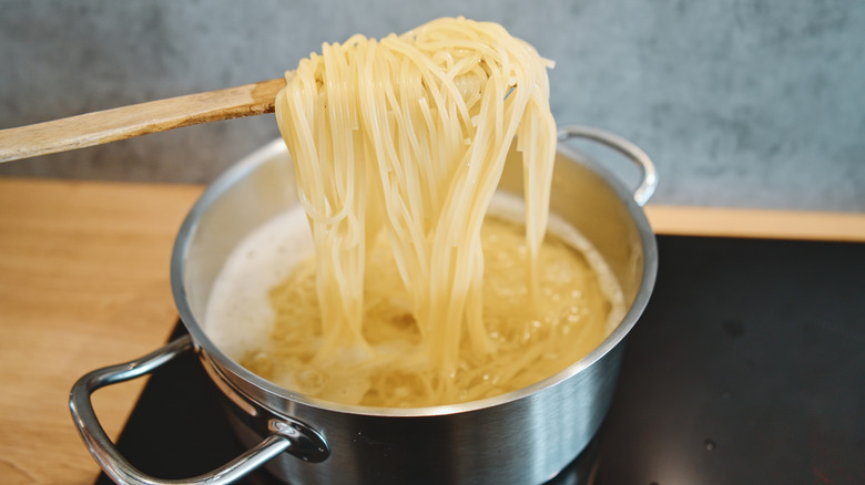 cooked spaghetti noodles being lifted out of a pot with a wooden spoon