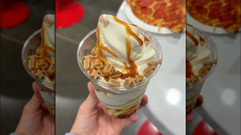Hand holding Caramel Churro Sundae from Costco food court with table and slice of pizza in background