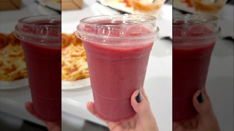 Hand holding Mixed Berry Smoothie from Costco food court in see-through plastic cup.