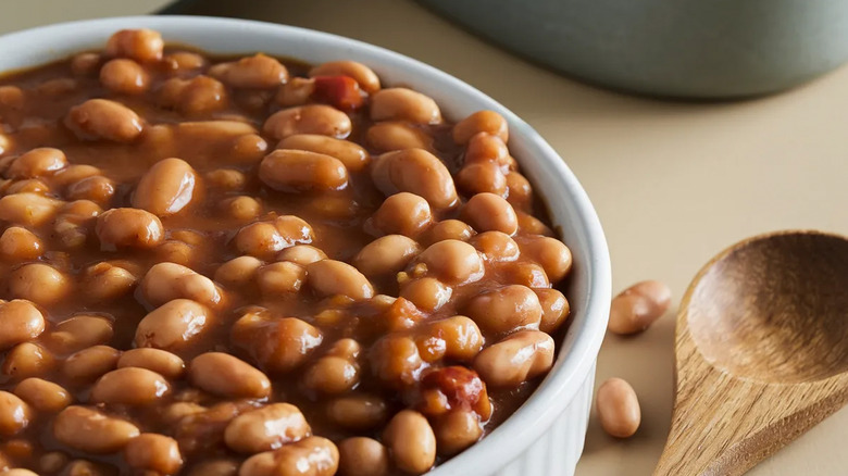 A bowl of baked beans is on a counter with a spoon next to it.