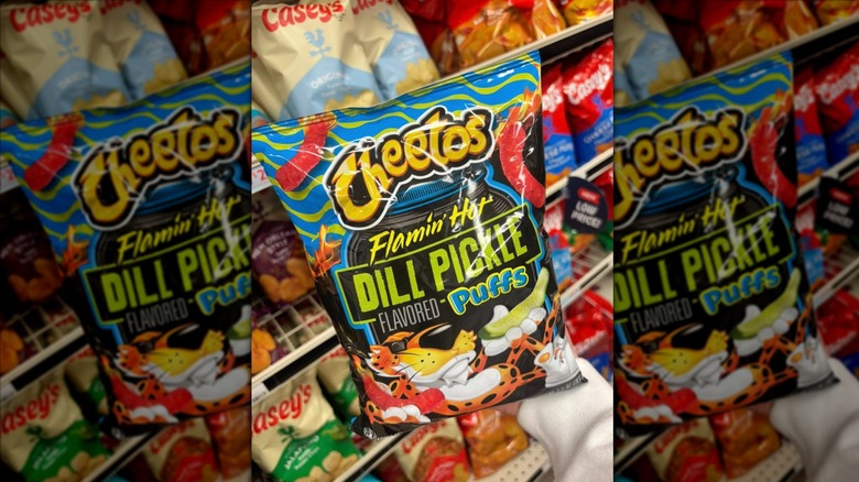 Hand holding a bag of Cheetos Flamin' Hot Dill Pickle Flavored Puffs in a store's chips aisle
