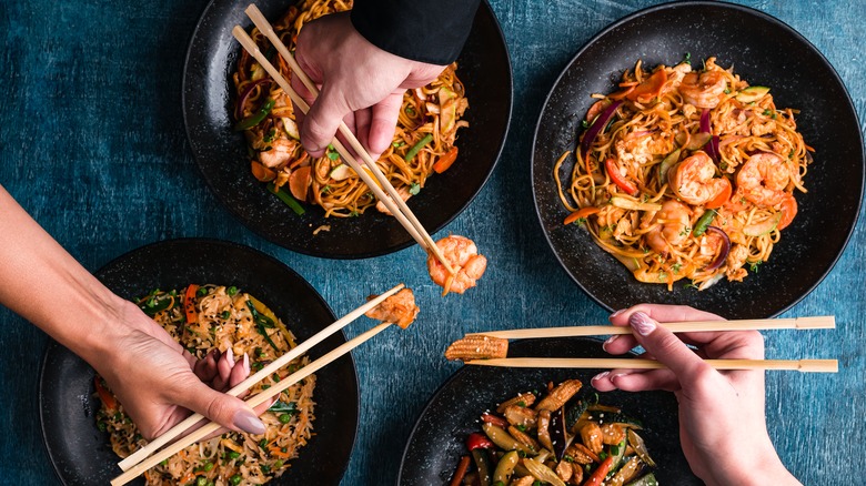 Hands holding chopsticks over noodle dishes