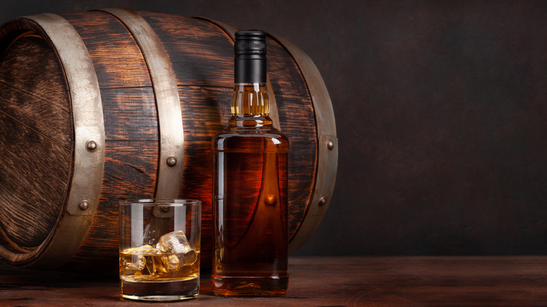 glass and bottle of bourbon in front of white oak barrel
