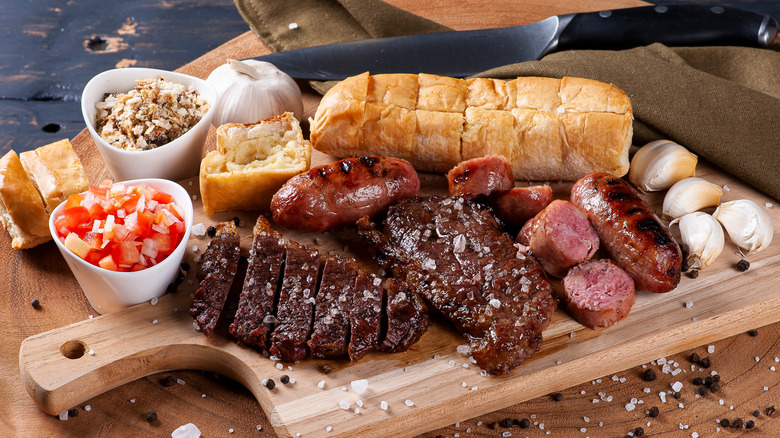 A Brazilian barbecue spread with sliced meat, sausage, bread, and garnishes