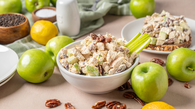 Bowl of chicken salad with celery, nuts, and apples next to ingredients
