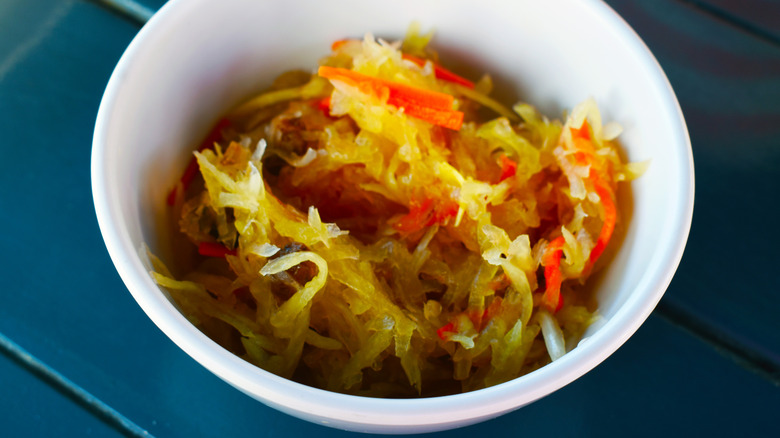 Pickled green papaya condiment is in a white bowl on a table.