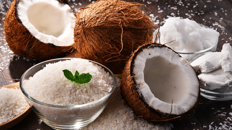 halved coconuts pictured next to bowls of coconut cream, oil, and shreds