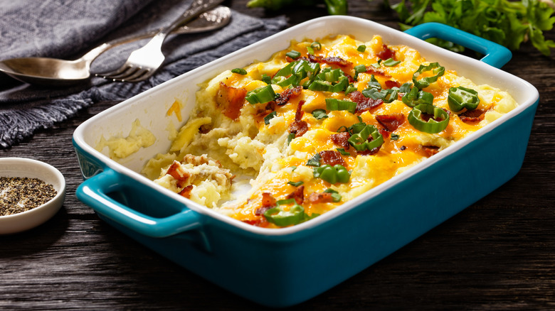 A blue casserole dish with loaded mashed potatoes, with some already served.