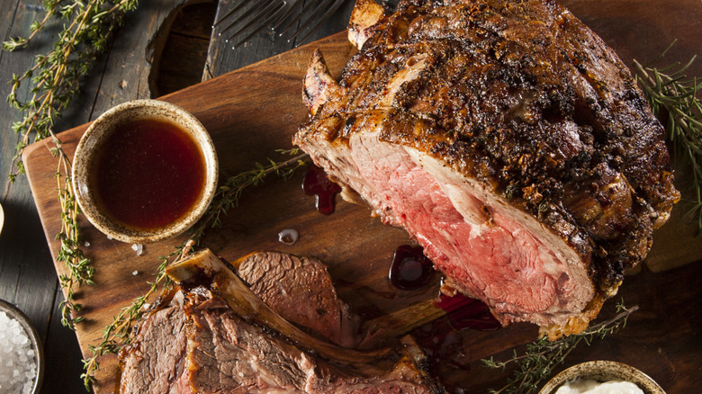 A prime rib roast sitting on a carving board alongside a bowl of meat drippings