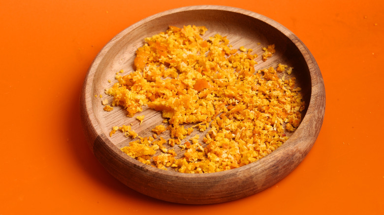 A wooden bowl of dried orange zest on an orange background