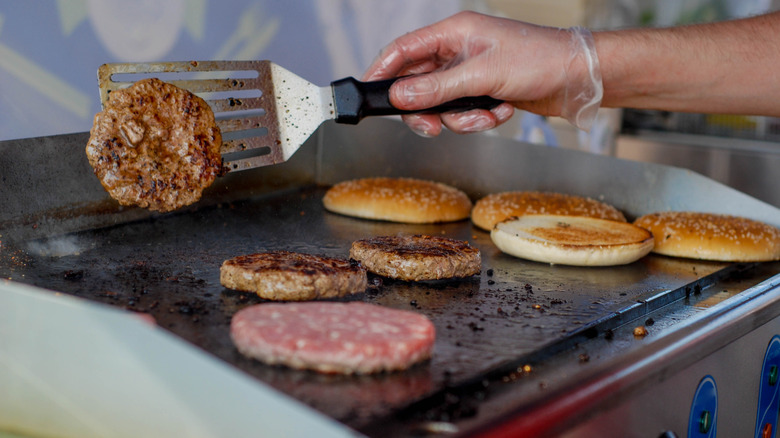 A person flips burgers on a flat top