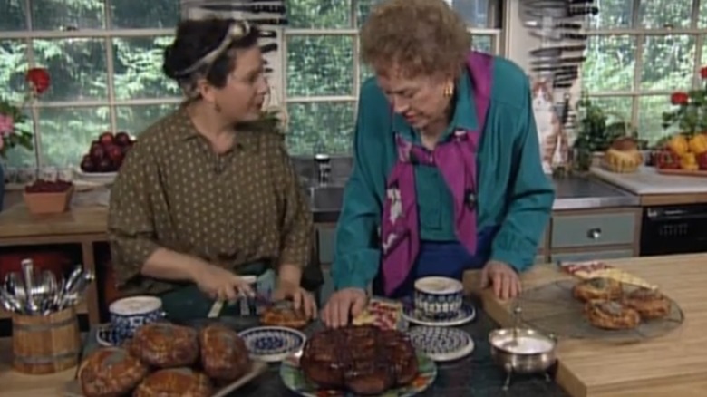 Julia Child and Nancy Silverton standing at a counter with plates of sticky buns and brioche