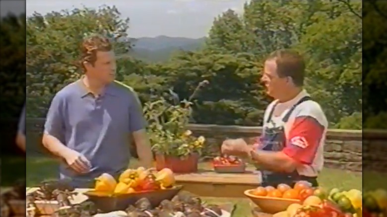 Bobby Flay and Jack McDavid in front of an outdoor table with fruit, vegetables, and lobster