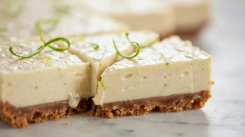 A creamy, sliced key lime cheesecake topped with curls of lime zest