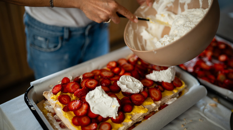someone putting whipped cream on strawberry lasagna