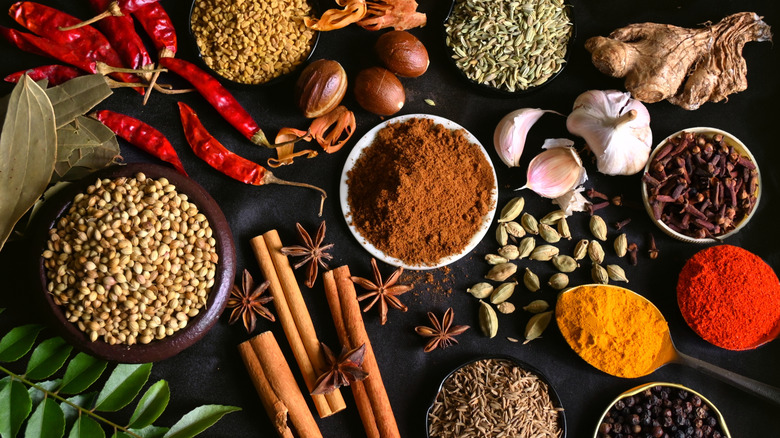 various whole spices in bowls, spoons, and strewn about