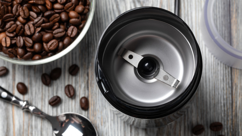an empty coffee grinder viewed from above with whole beans in the background