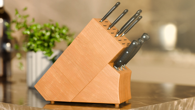 A wooden knife block on a counter full of knives