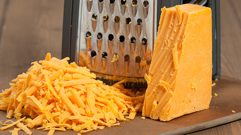 Shredded cheese block with shreds next to it in front of a metal grater