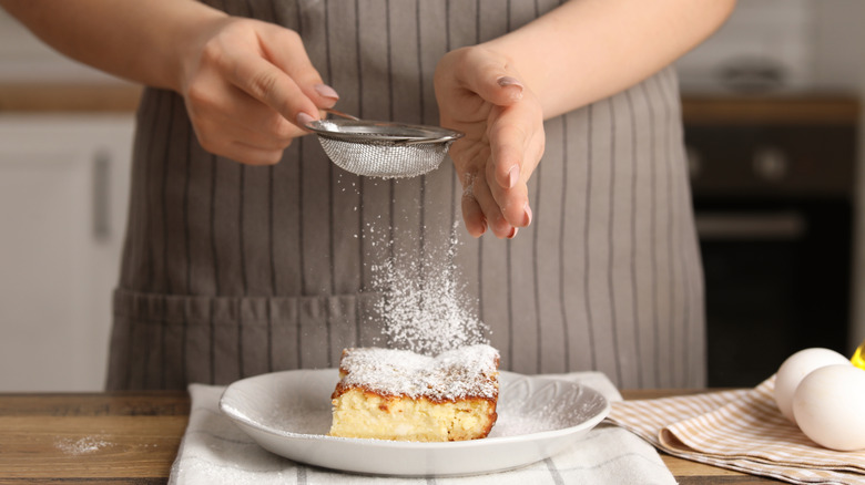 Sifting powdered sugar over slice of cake