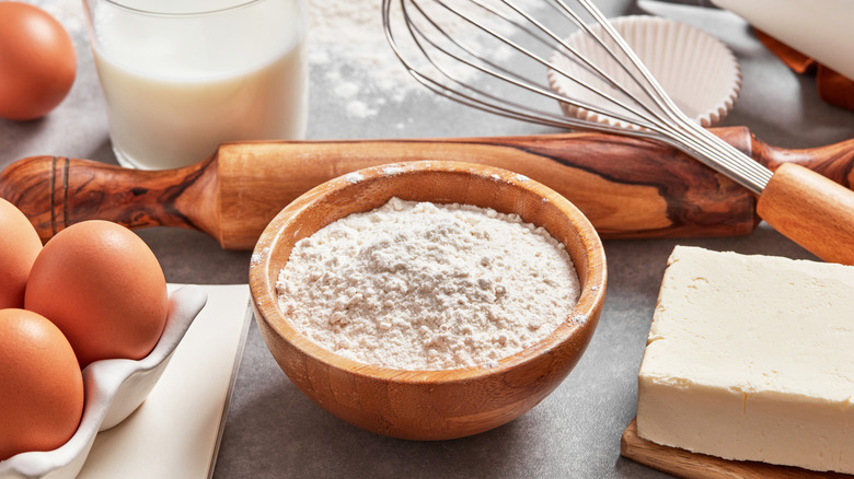 a bowl of flour surrounded by baking ingredients and utensils