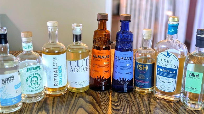 Nine bottles of non-alcoholic tequila lined up on a wooden table