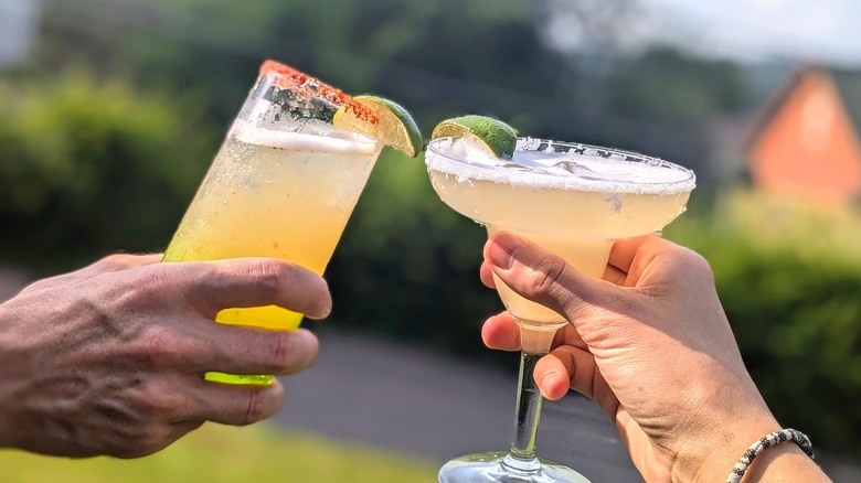 Two hands cheers with margaritas in two different glasses