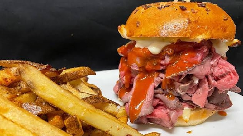 Roast beef sandwich with cheese and sauce next to fries