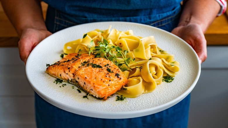 person holding a plate of creamy salmon pasta