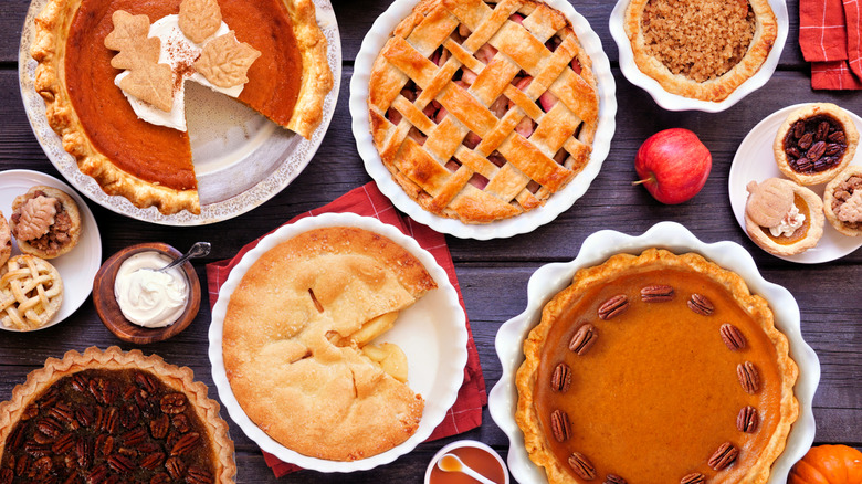 A table set with multiple different pies including pumpkin, apple, pecan, and several more