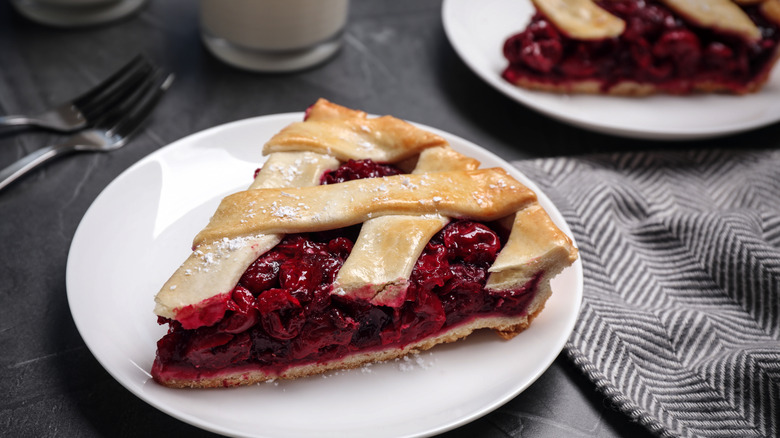 A slice of lattice cherry pie sitting on a white plate on a table