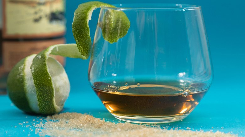 glass of rum with lime peel and scattered brown sugar