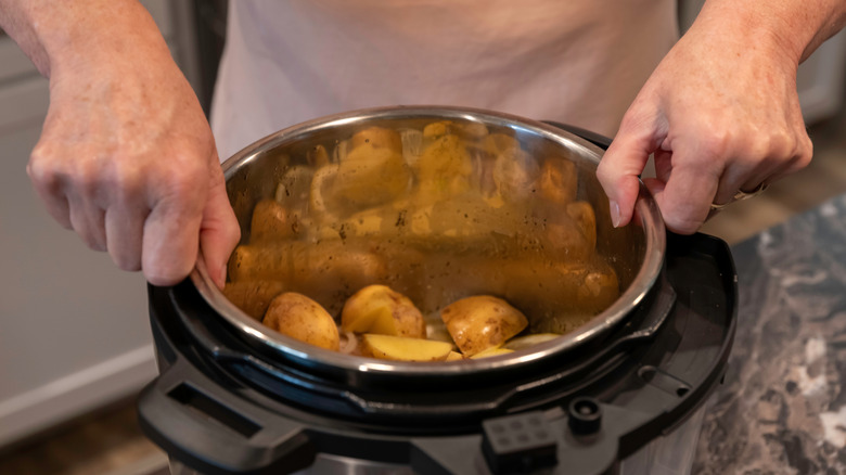 A person holds the insert of a slow cooker filled with cut potatoes.