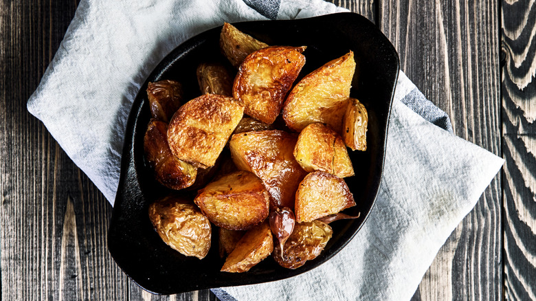 A bowl of golden, crispy roasted potatoes sits on a table.