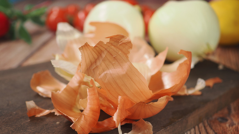 A close-up of onions and onion peels on a cutting board.