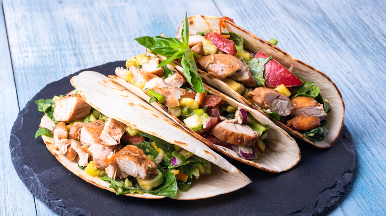 Three turkey meat tacos on a plate with avocado, onions, tomatoes, herbs