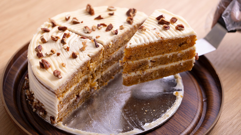Carrot cake sitting on a plate with a slice being lifted out.