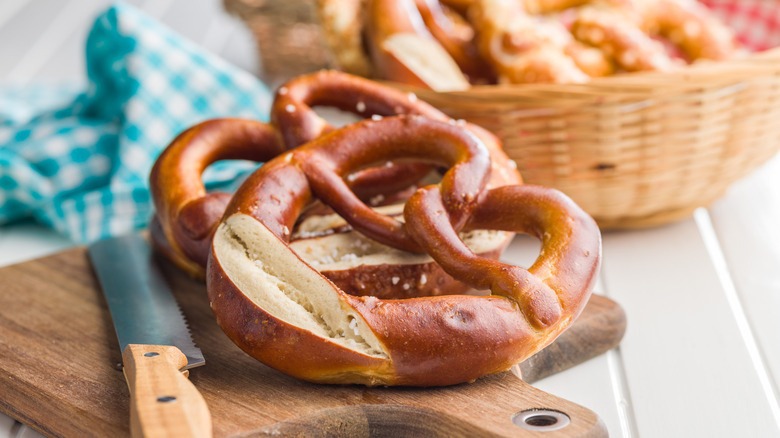A large soft Bavarian pretzel on a cutting board with a bread knife