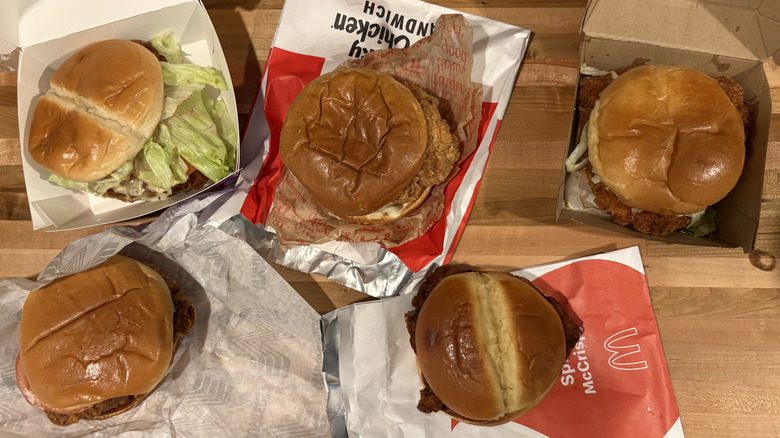 Various fast food fried chicken sandwiches with wrappers on table