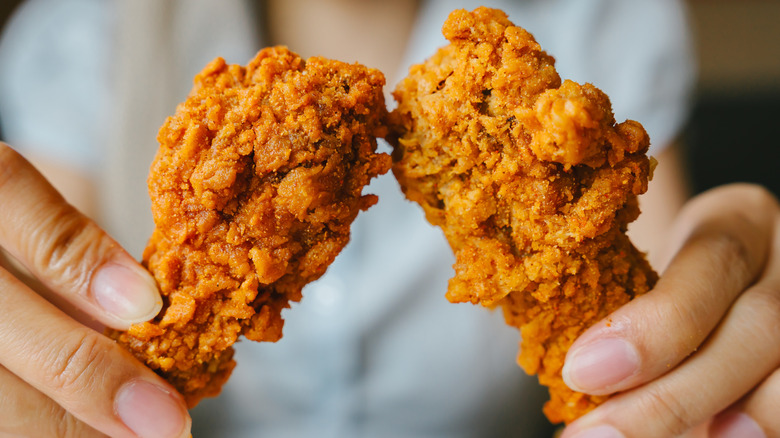 Hands holding two pieces of fried chicken
