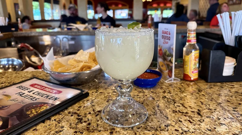 A Grande On the Border Classic Margarita on a marble bar with chips, salsa, and menu