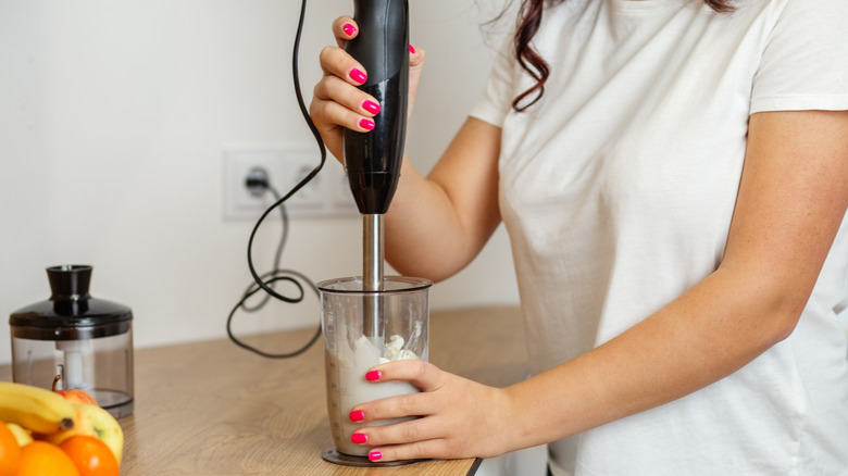 a person in a white shirt using an immersion blender