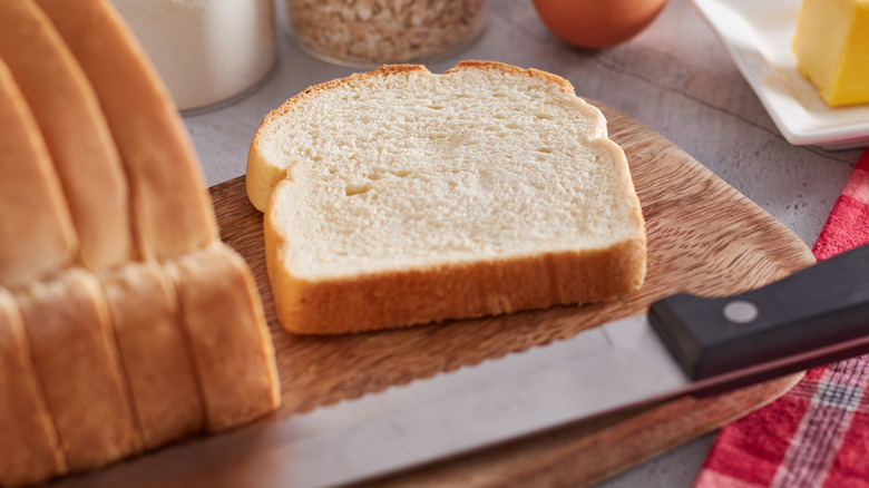 A loaf of sliced bread on a cutting board next to a bread knife